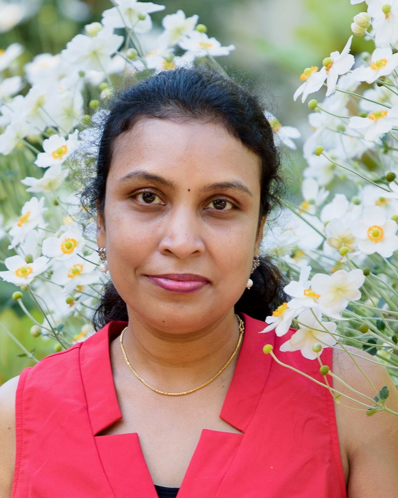 Madhu — owner of Madhu's Home Daycare — smiling gently, surrounded by white anemone flowers