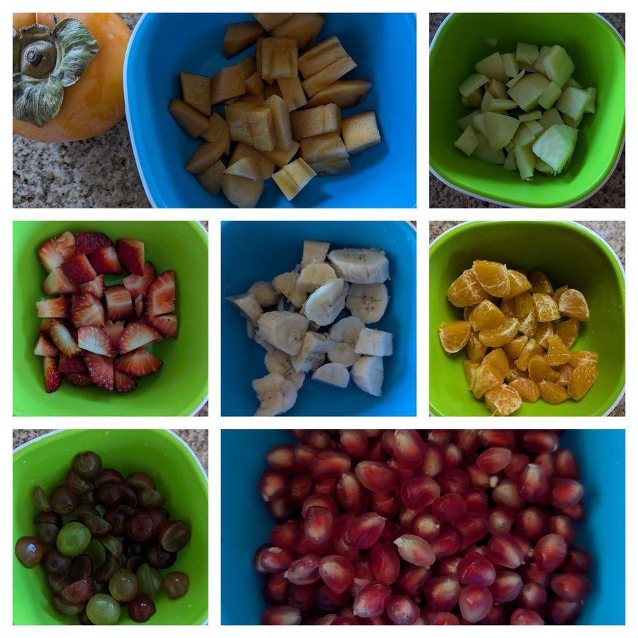 Fresh-cut fruit prepped for daily snacks — persimmon, apple, strawberries, bananas, mandarins, grapes, and pomegranate served in colorful bowls